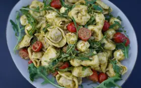 Ein köstlicher Tortellini-Salat mit Pesto, Kirschtomaten und Mozzarella-Kugeln, garniert mit Rucola.