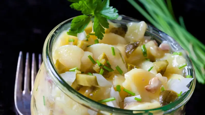 Ein köstlicher Kartoffelsalat ohne Mayo, mit Gurken und frischen Kräutern, serviert in einem Glas.
